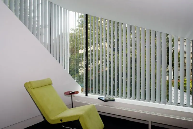 Stores verticaux clairs le long d'un mur vitré, chaise longue vert lime