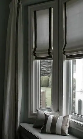 Stores romains gris foncé bordés de noir et rideau gris sur fenêtre