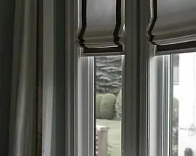 Stores romains gris à bordure noire et rideau gris sur fenêtres